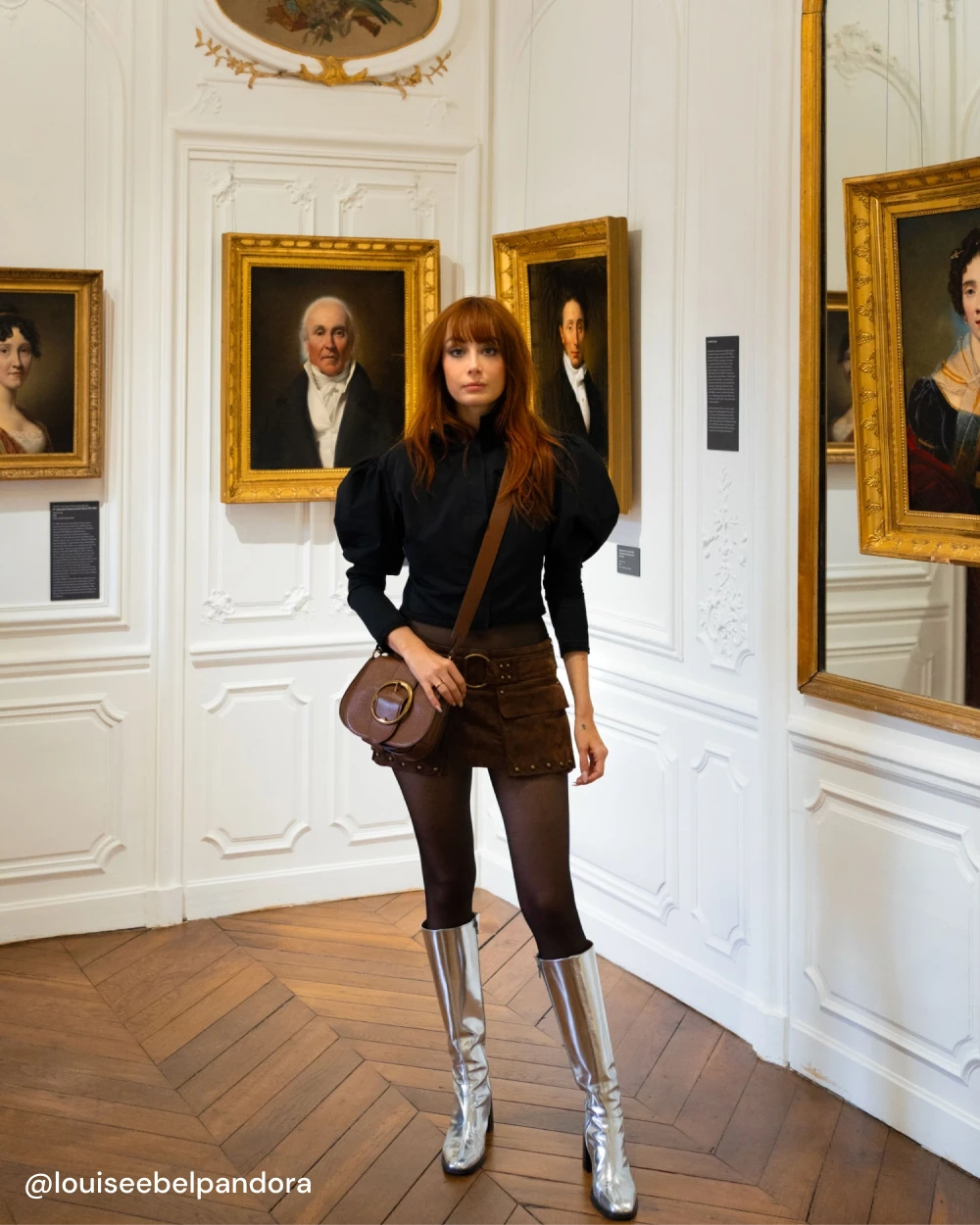 Louise porte les bottes CRISTOBAL à talon en cuir argent avec un short et une blouse noire